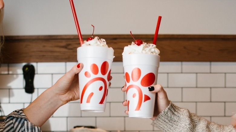 Two people cheersing with Chick-fil-A milkshakes