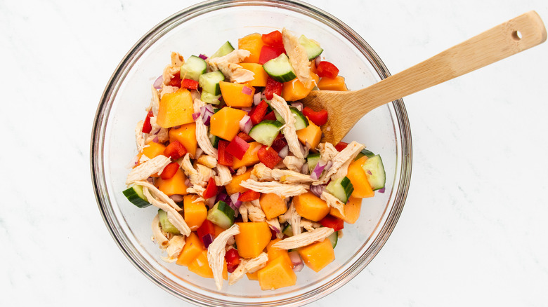 mixing chicken melon salad in bowl