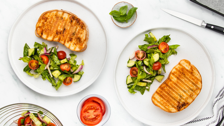 two chicken caprese panini on plates with salad