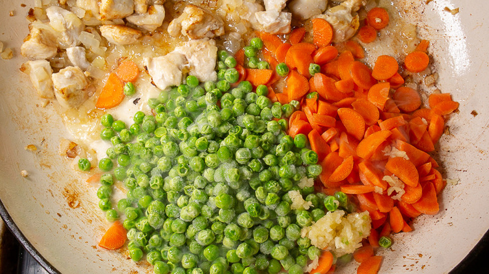 peas and carrots added to a hot pan for chicken fried rice