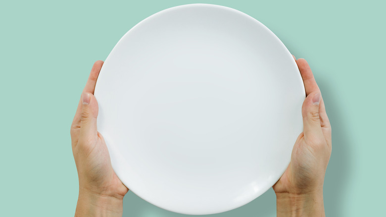 Hands holding empty white plate on blue background