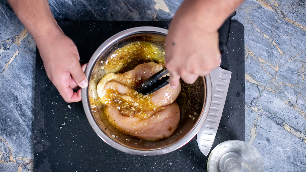 hands mixing chicken pieces into marinade in a metal bowl