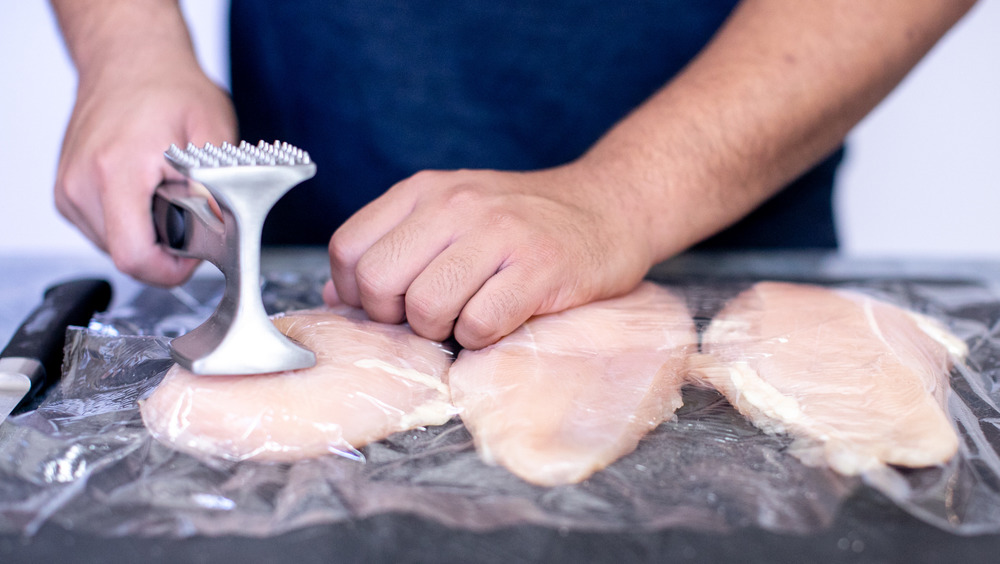 hands using a meat tenderizer to pound chicken breasts