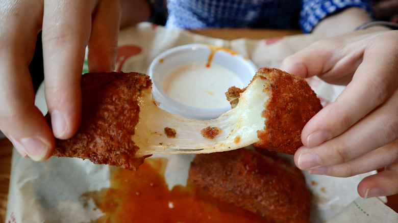 hands holding halves of mozzarella stick with cheese pull