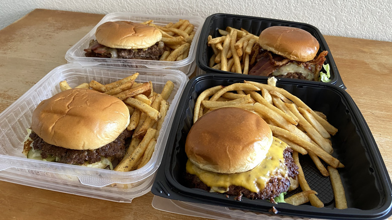 Four burgers with fries sit in takeout boxes