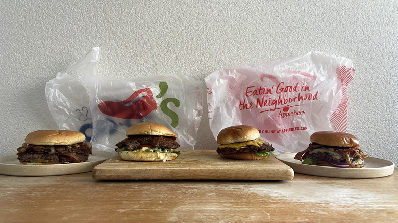 Four burgers with restaurant bags lined up on a table