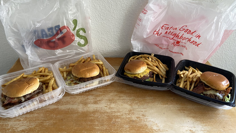 Four burgers in containers with the restaurant bags behind them