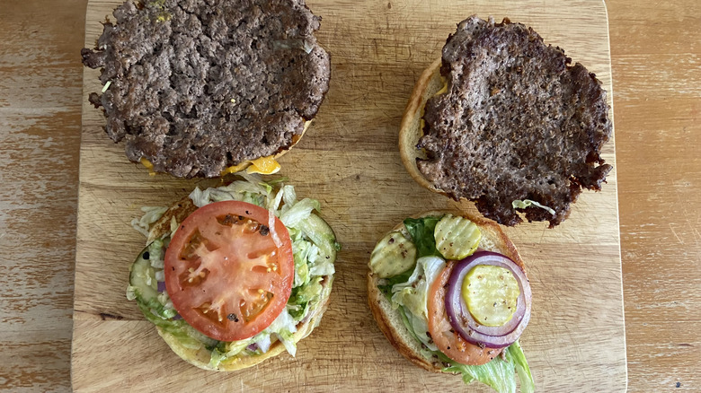 Two cheeseburgers are open faced with visible veggies