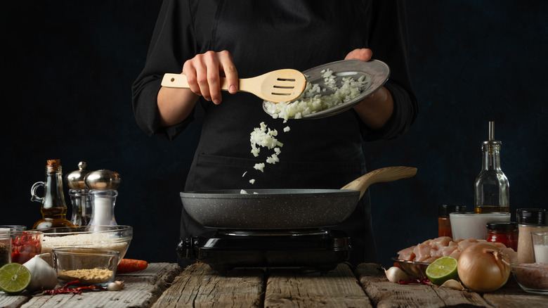 chef spooning onions into frying pan