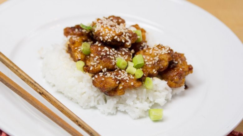 sesame chicken with rice on white plate with chopsticks