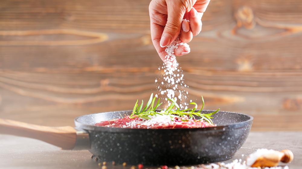 Woman adding salt to meat