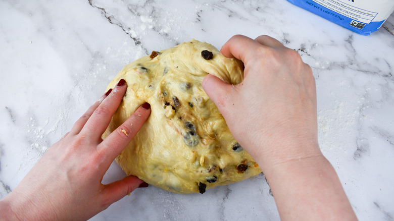 hands folding dried fruit into panettone dough