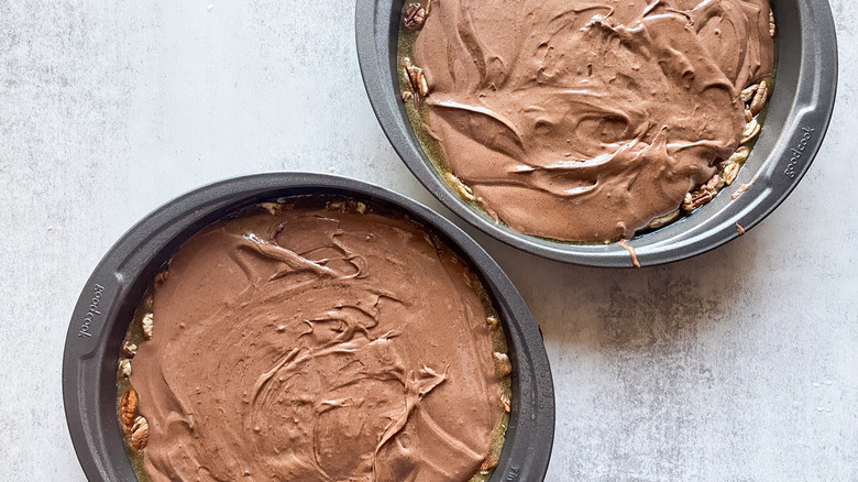 chocolate cake batter spread across pralines in two round cake pans