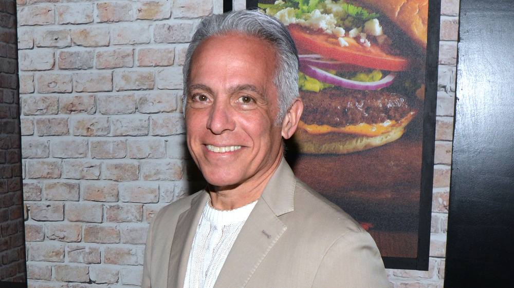 Geoffrey Zakarian in front of a picture of a burger