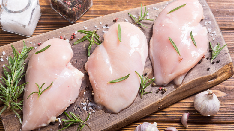 Raw chicken breasts on wooden platter