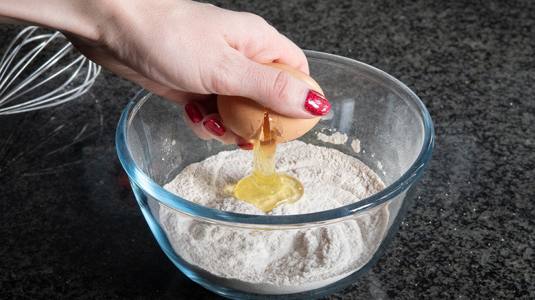 hand cracking egg in bowl of flour