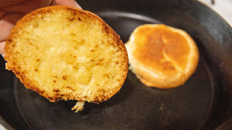 two sides of a buttered bun toasting in an iron skillet