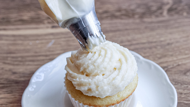 piping buttercream frosting on cupcake