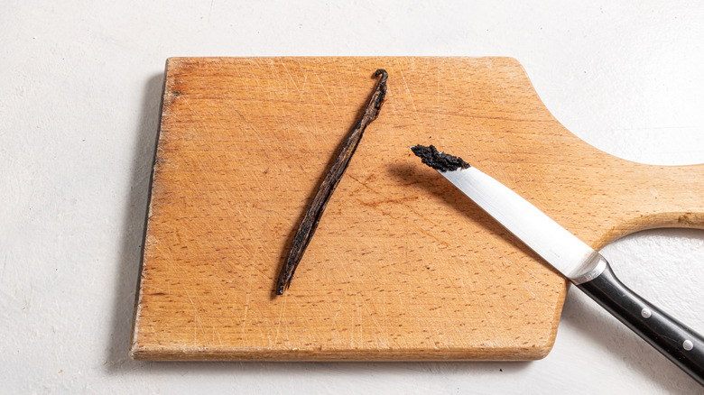 Cutting board with vanilla bean and a knife with vanilla seeds scraped out of the vanilla bean