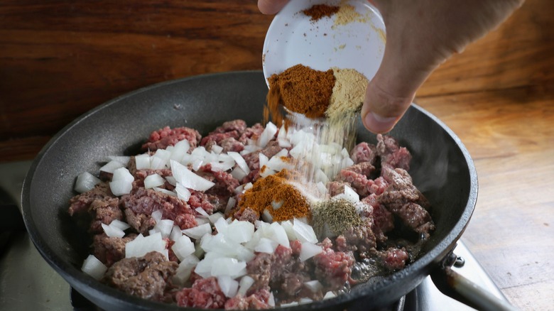 pouring spices over skillet of beef