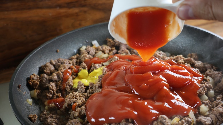 adding ketchup to skillet of ground beef