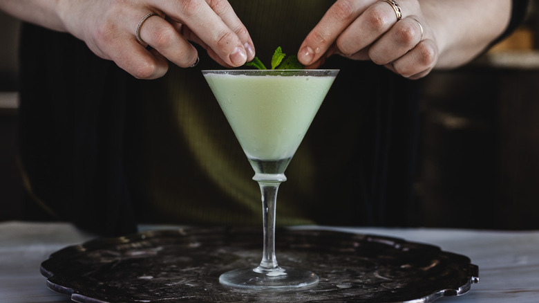 hands placing mint on cocktail