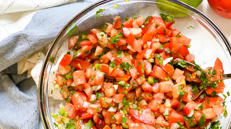 Overhead shot of a metal spoon mixing pico de gallo in a glass bowl