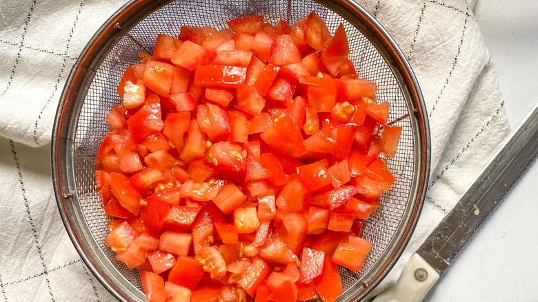 Overhead shot of a colander filled with diced up tomatoes next to a knife