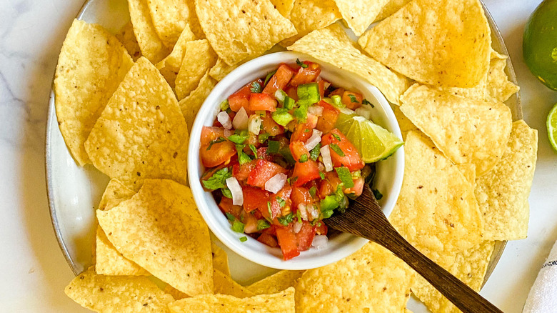 Overhead of shot of a bowl of pico de gallo surrounded by tortilla chips