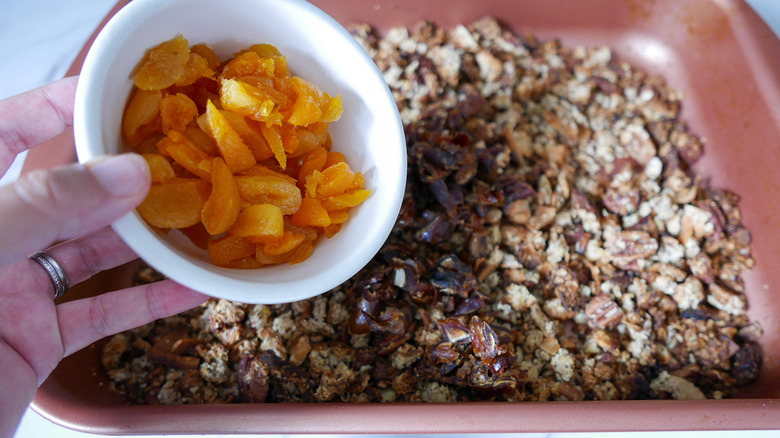 hand holding dried apricots over muesli