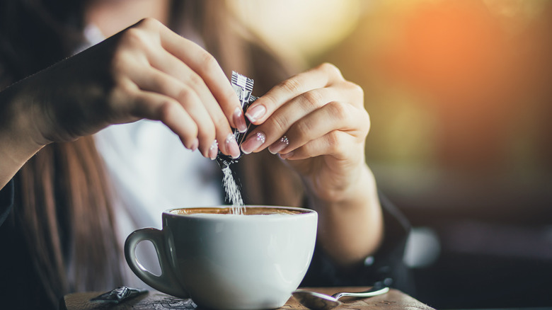 Woman pouring sugar into coffee