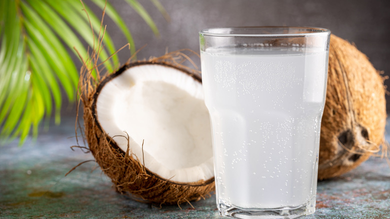 glass of coconut water with fresh coconut behind