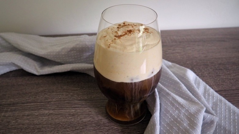 A glass of dark cold brew coffee topped with a large amount of whipped pumpkin-flavored foam