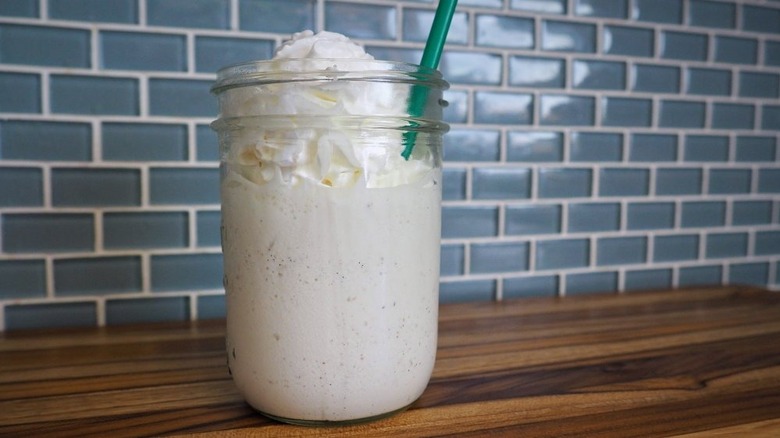 A glass mason jar filled with vanilla bean coffee frozen frappuccino with a green straw