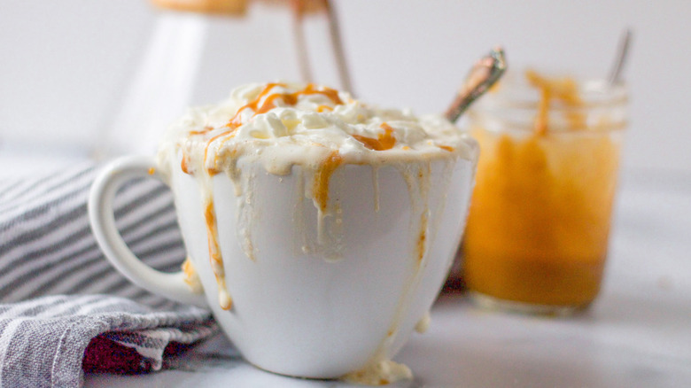 A coffee mug overflowing with a latte, topped with whipped cream