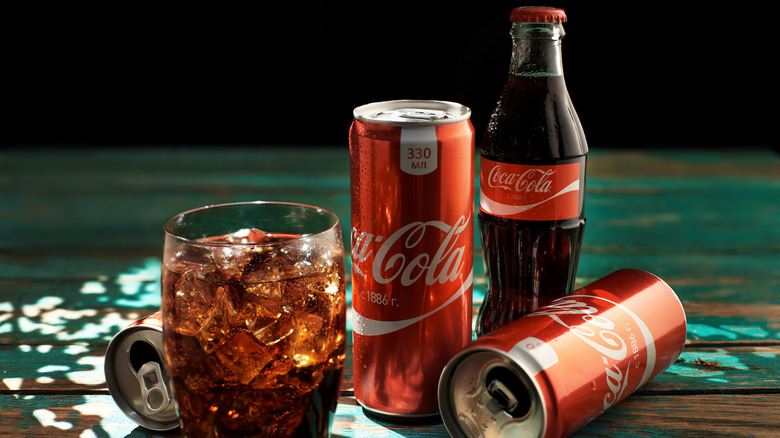 Coca-Cola in a glass with cans and bottle