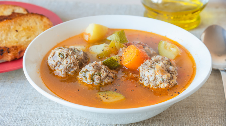 Meatball soup in a bowl with a plate of toast nearby.