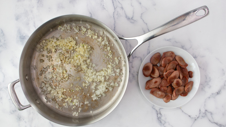 Diced onions and garlic in skillet with bowl of seared hot dog slices