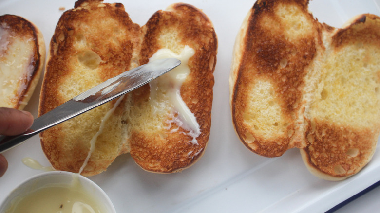 A person applying condensed milk on the sliced brioche rolls.