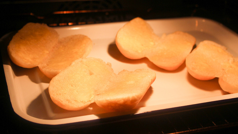 Sliced brioche rolls placed in a tray inside an oven.