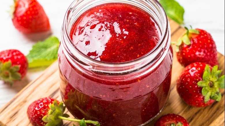 Strawberry jam in a glass jar surrounded by fresh strawberries