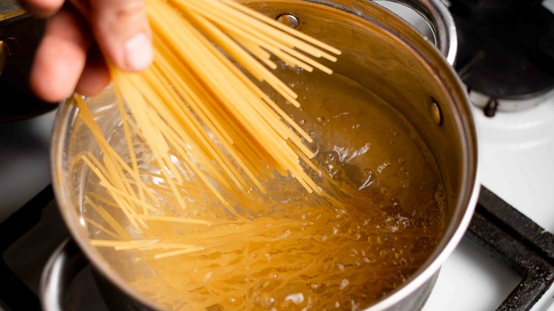 Hand putting spaghetti into boiling water