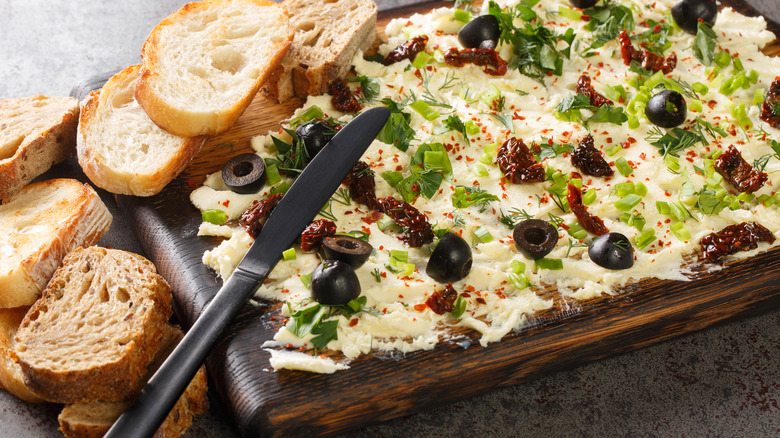 Butter board with olives, peppers, and herbs