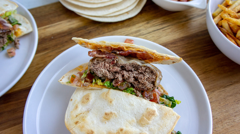 a burger between two tortillas with bacon, cheese, lettuce, and pico