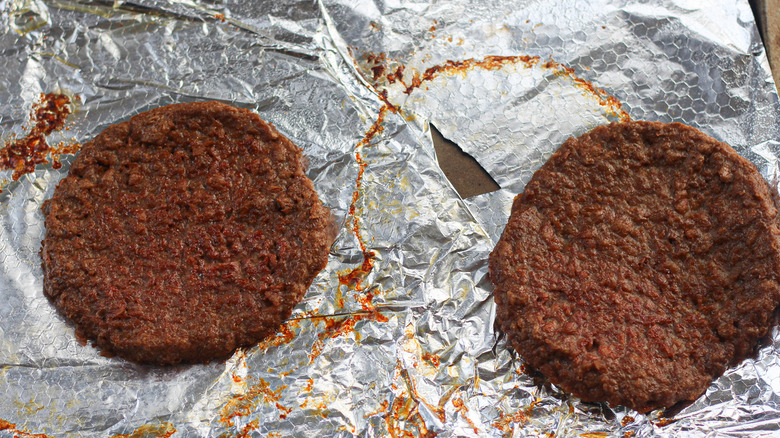 Two burger patties on a foil-lined baking tray.