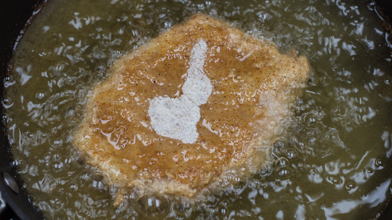 A breaded chicken breast frying