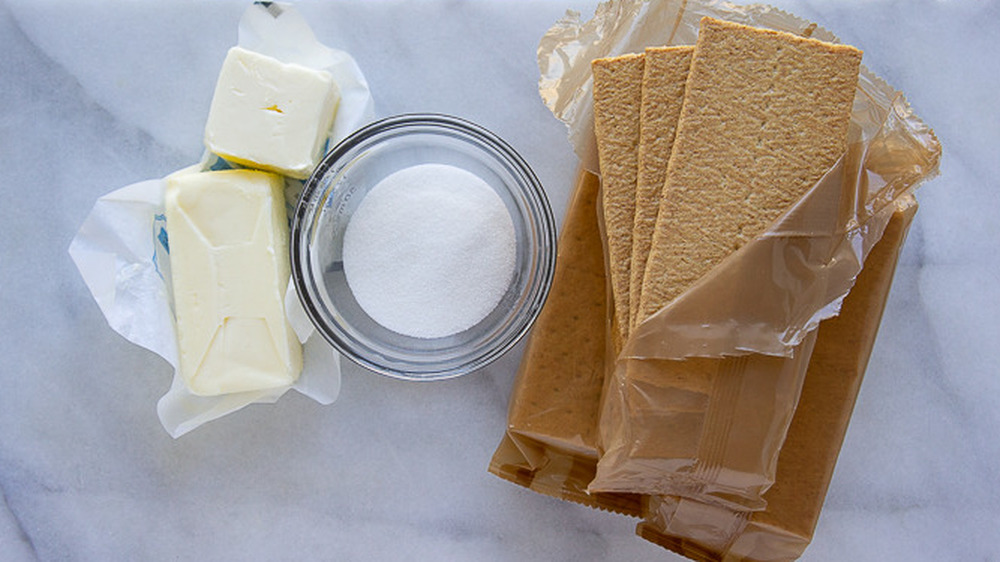 bowl of sugar, graham crackers, and cubes of butter on a white cutting board