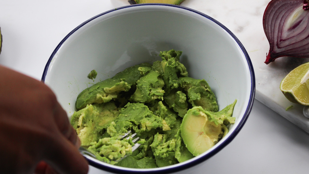 avocados being mashed with a fork in white bowl