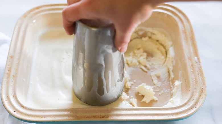 A hand holding a cocktail shaker on a sheet of ice cream