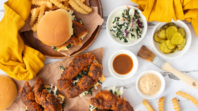 Various chicken sandwiches, bowls of sauce, coleslaw, and pickles